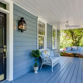A blue porch with a wicker chair and swing
